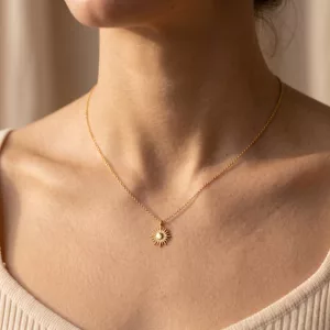 Aurore Pendant Necklace worn at the collarbone: a gold-plated chain with a sunburst pendant set with a pearl