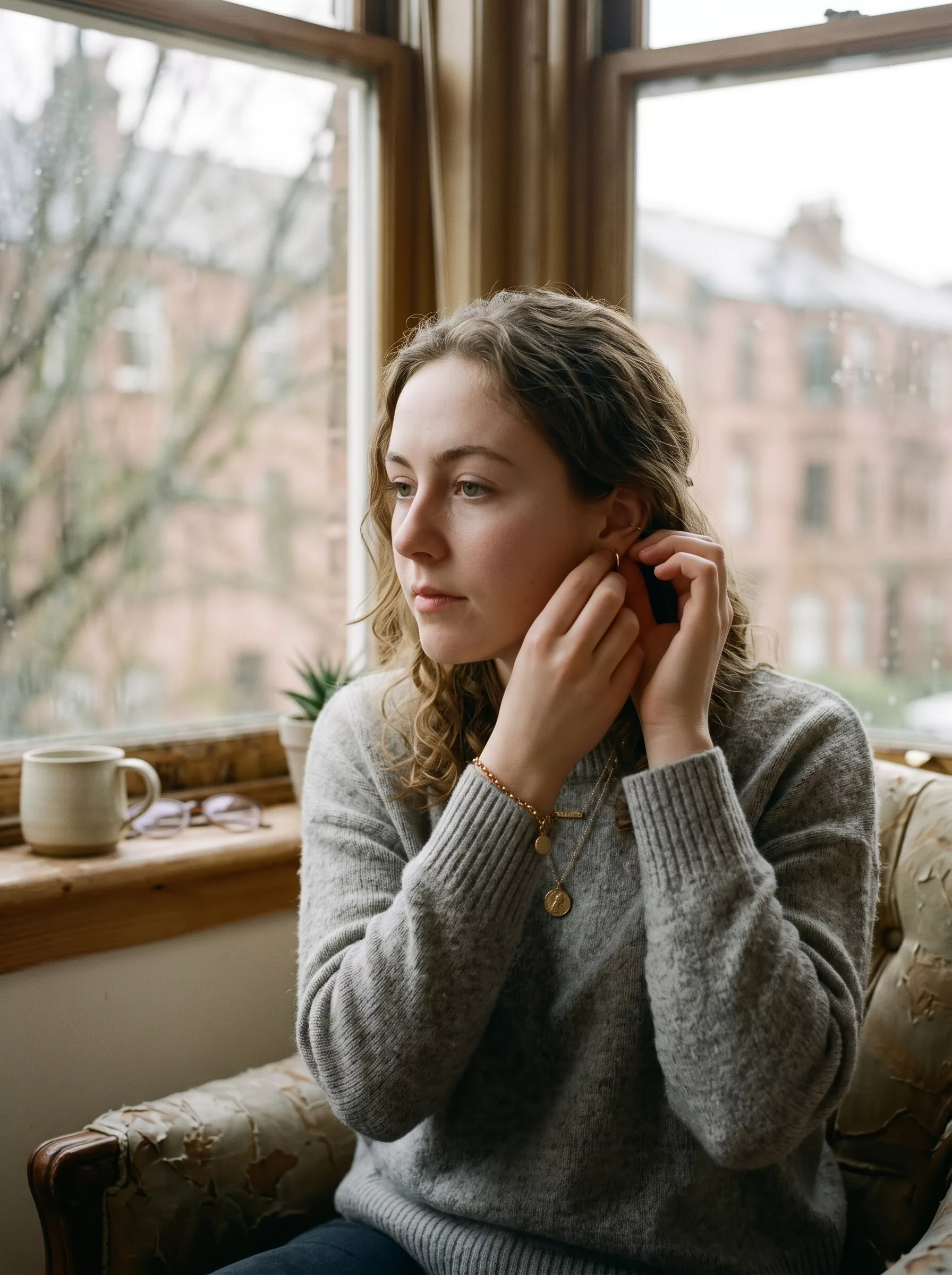 Woman putting on a gold earring by the window